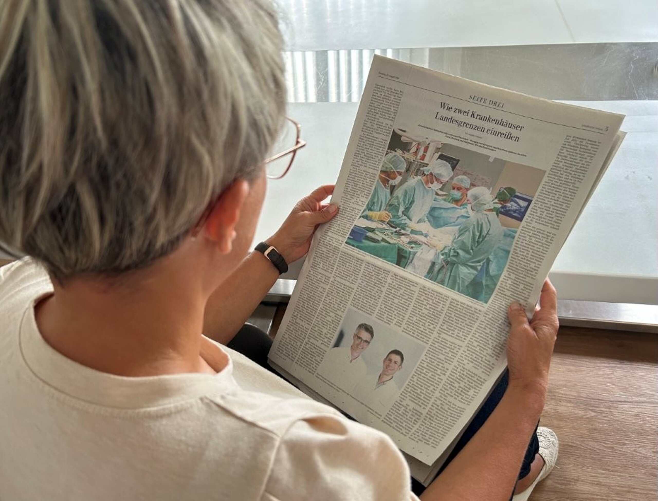 Frau liest in der Schwäbischen Zeitung vom 25. August 2026 den Artikel „Wie zwei Krankenhäuser Landesgrenzen einreißen“.