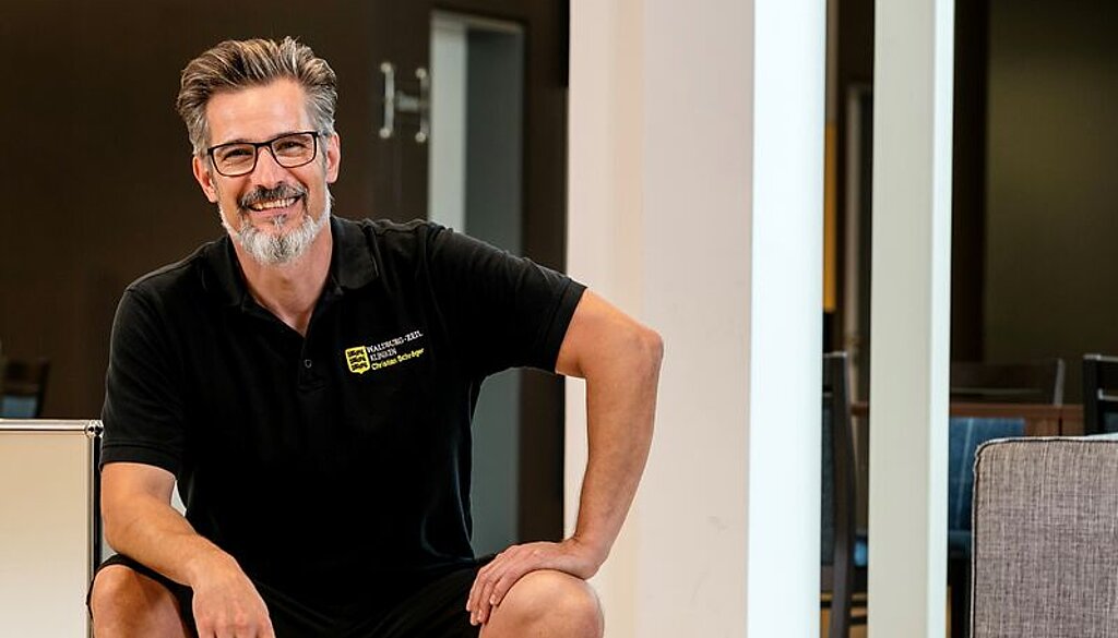 Christian Schröger sitzt und lacht in die Kamera.