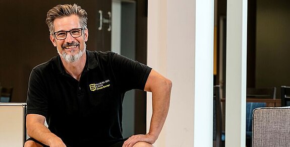 Christian Schröger sitzt und lacht in die Kamera.