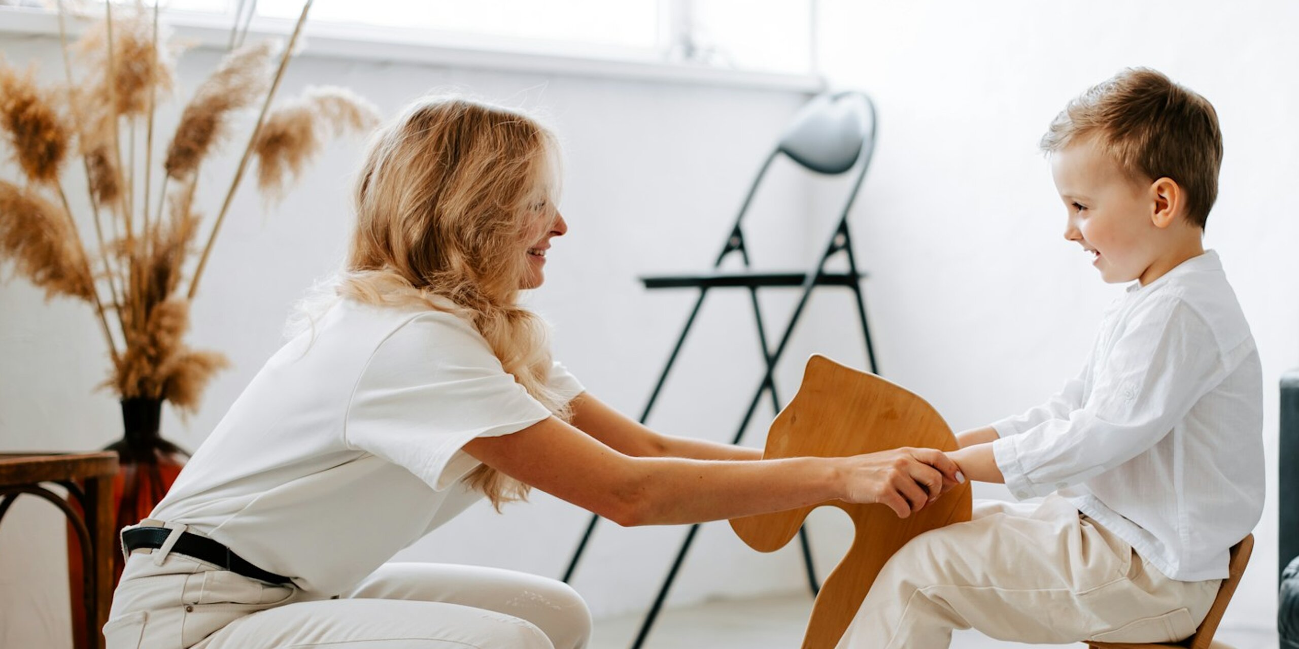 Eine freundliche Ärztin hält die Hände eines Jungen auf einem Schaukelpferd.