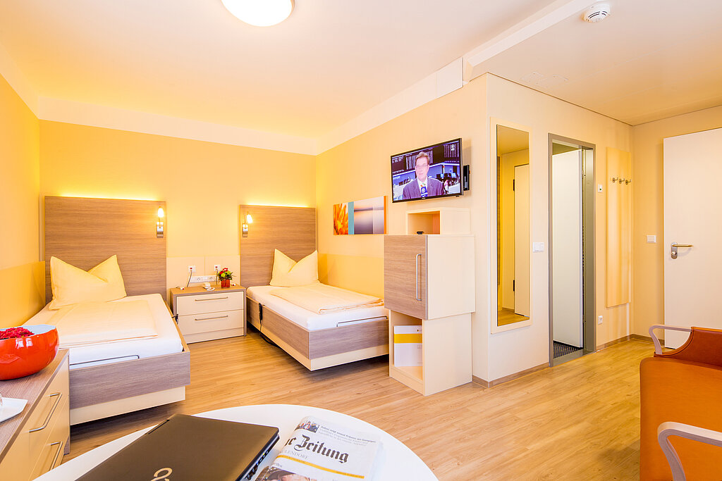 Helles Komfort-Doppelzimmer der KIH mit zwei Betten und einem Sitzbereich 
