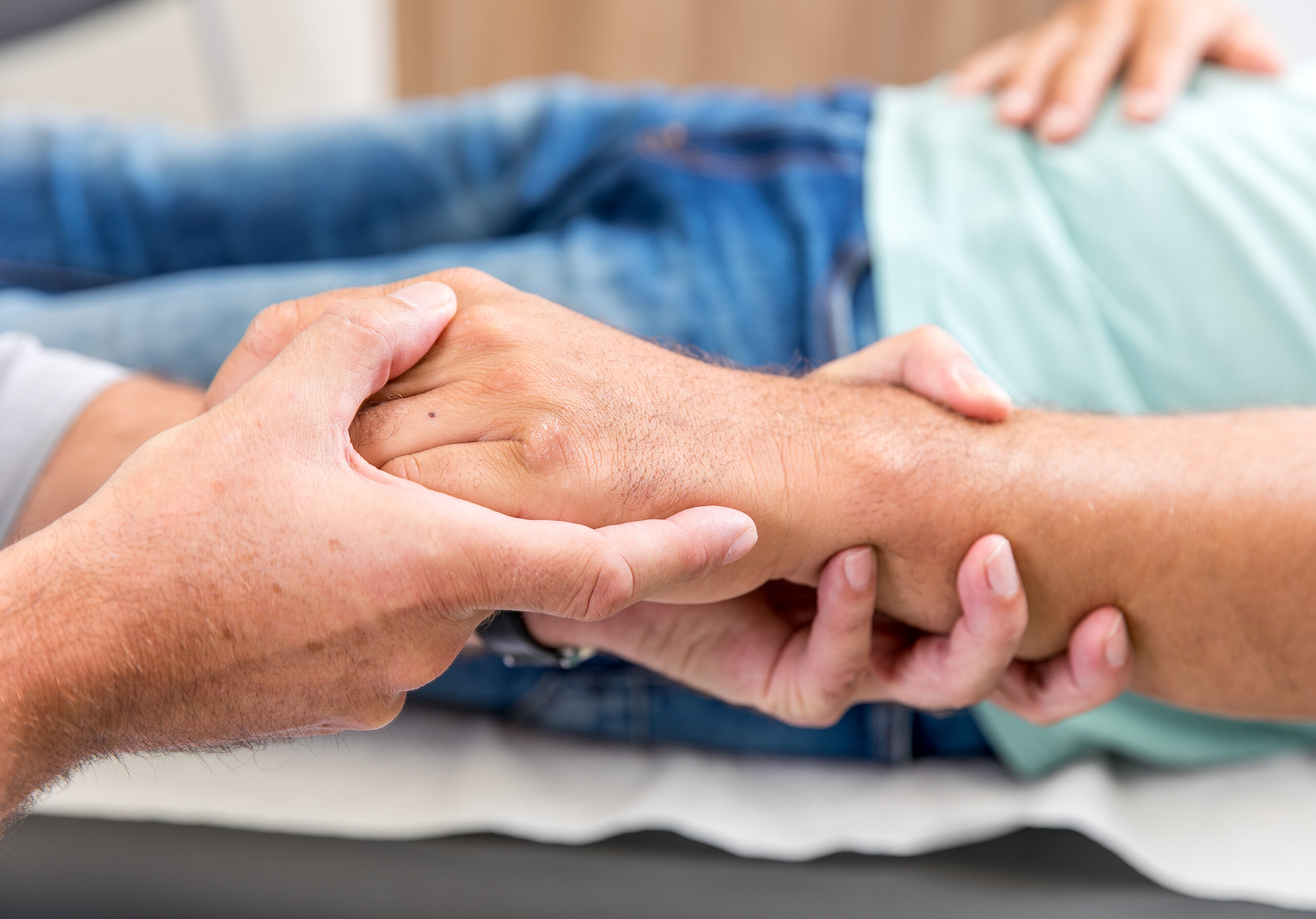 Zwei Personen halten sich die Hände, Symbol für Fürsorge, Vertrauen und menschliche Nähe.