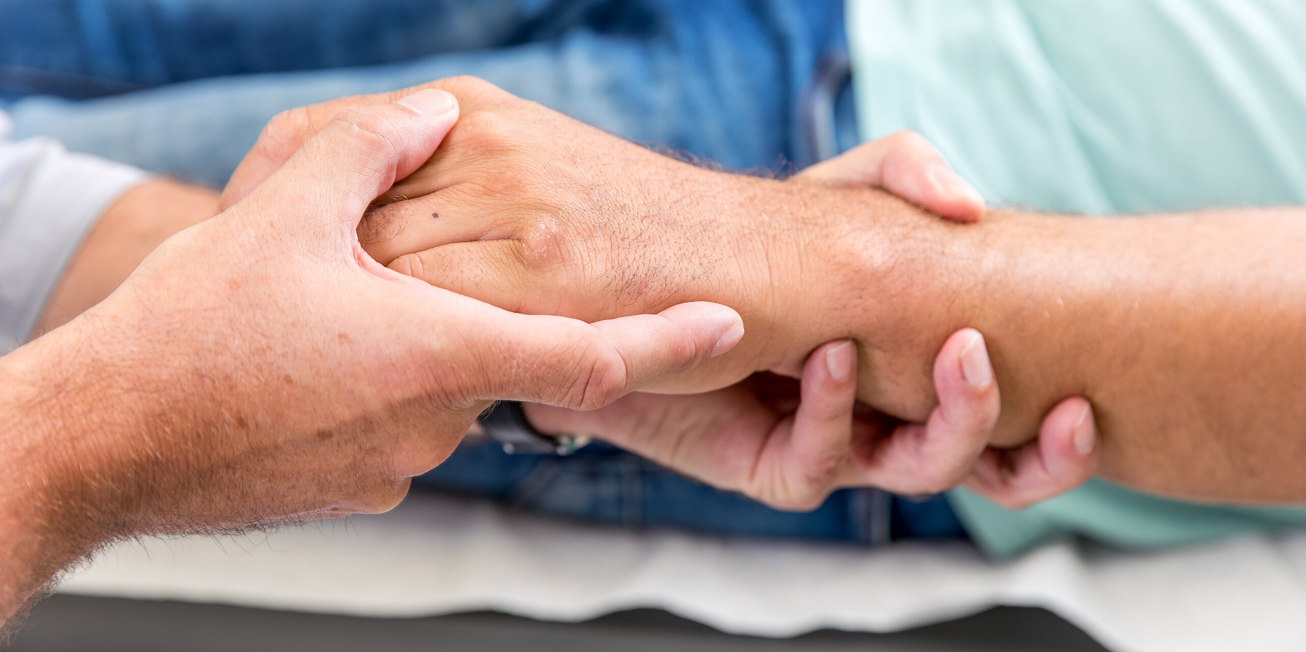 Zwei Personen halten sich die Hände, Symbol für Fürsorge, Vertrauen und menschliche Nähe.