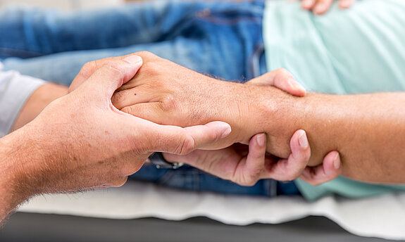 Zwei Personen halten sich die Hände, Symbol für Fürsorge, Vertrauen und menschliche Nähe.
