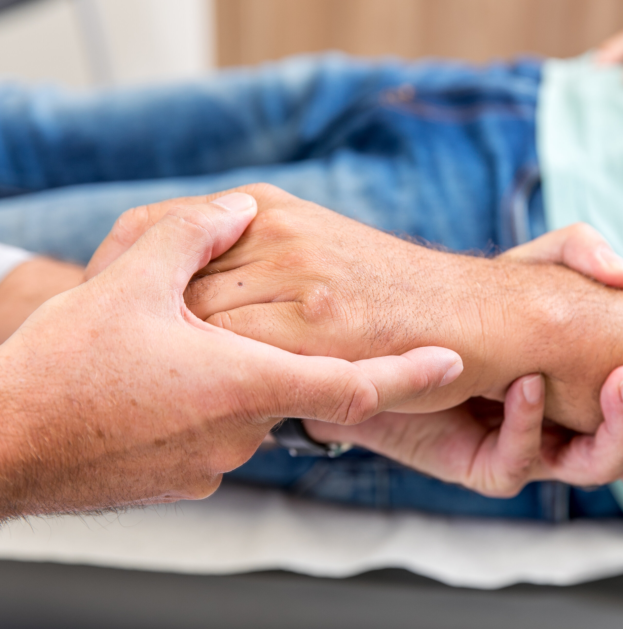 Zwei Personen halten sich die Hände, Symbol für Fürsorge, Vertrauen und menschliche Nähe.