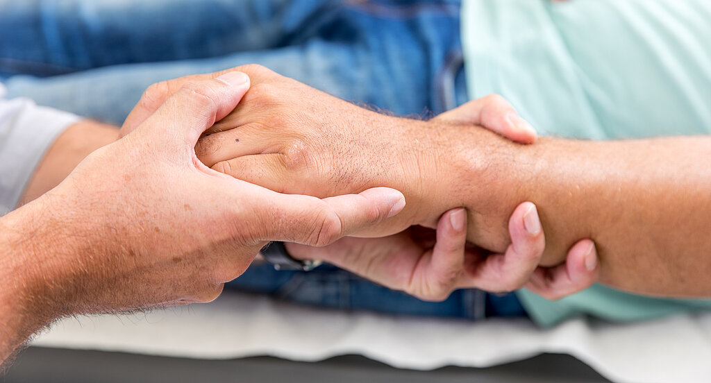 Zwei Personen halten sich die Hände, Symbol für Fürsorge, Vertrauen und menschliche Nähe.
