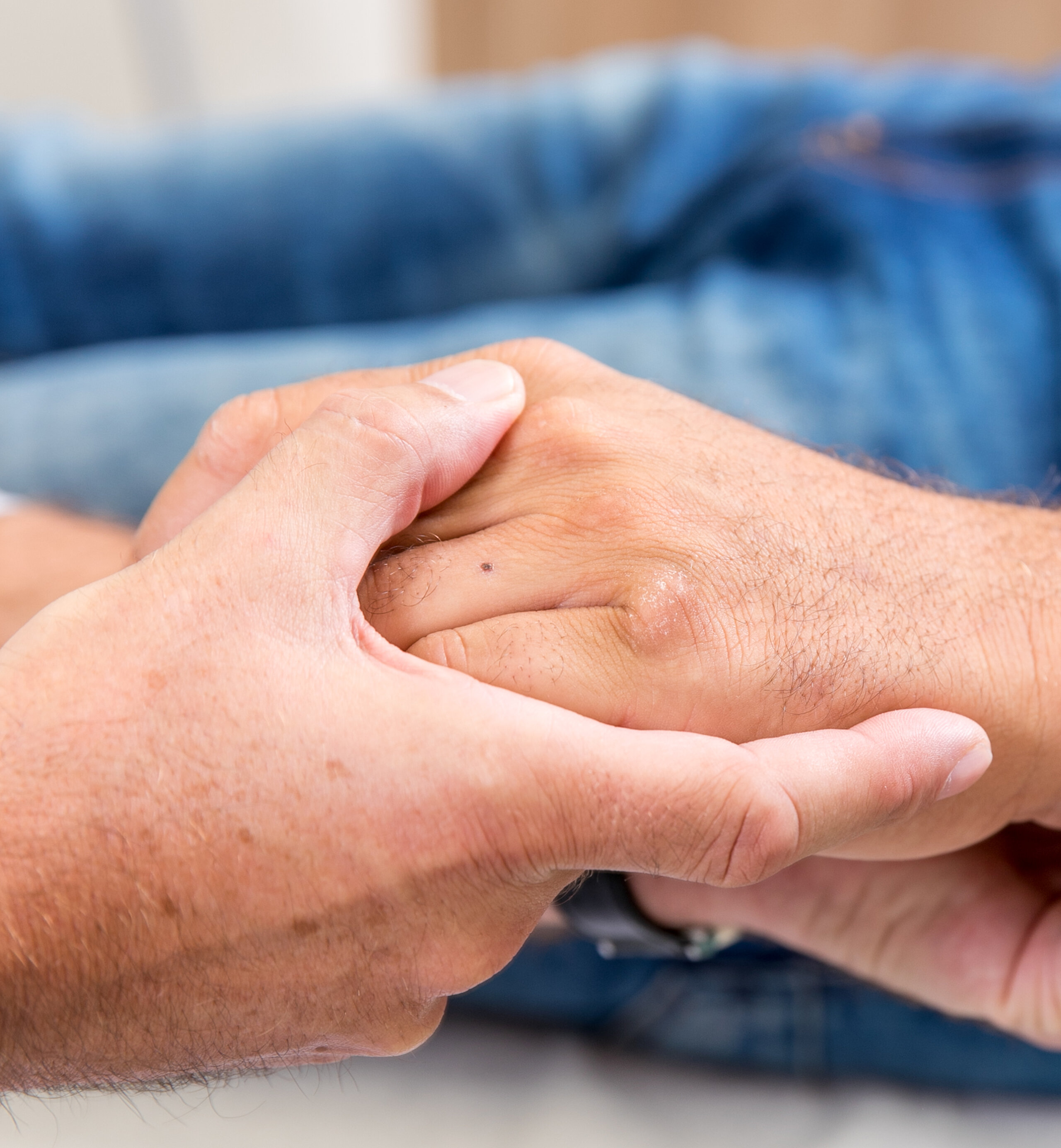 Zwei Personen halten sich die Hände, Symbol für Fürsorge, Vertrauen und menschliche Nähe.