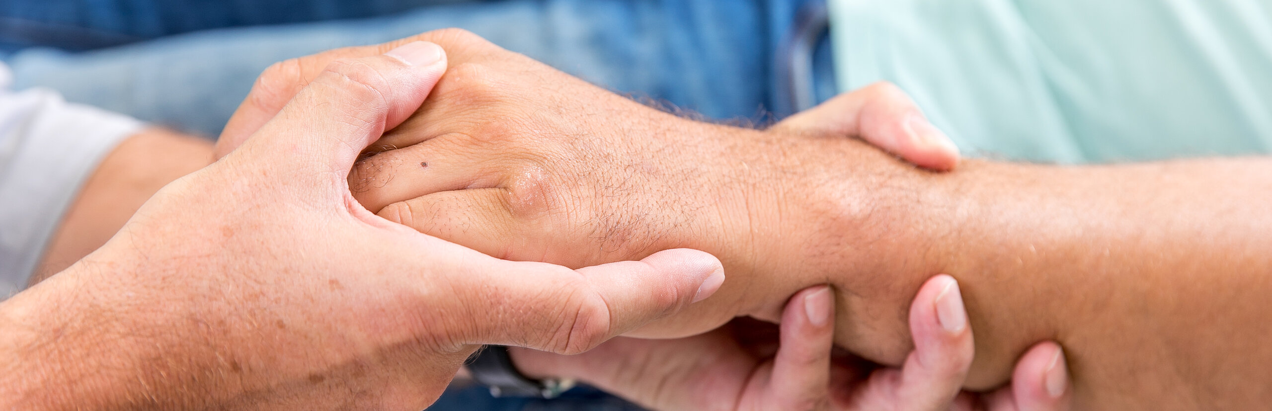 Zwei Personen halten sich die Hände, Symbol für Fürsorge, Vertrauen und menschliche Nähe.