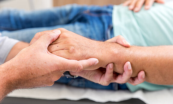 Zwei Personen halten sich die Hände, Symbol für Fürsorge, Vertrauen und menschliche Nähe.
