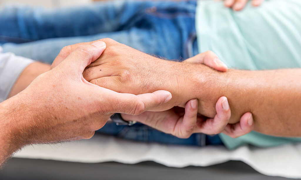 Zwei Personen halten sich die Hände, Symbol für Fürsorge, Vertrauen und menschliche Nähe.
