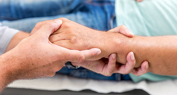 Zwei Personen halten sich die Hände, Symbol für Fürsorge, Vertrauen und menschliche Nähe.