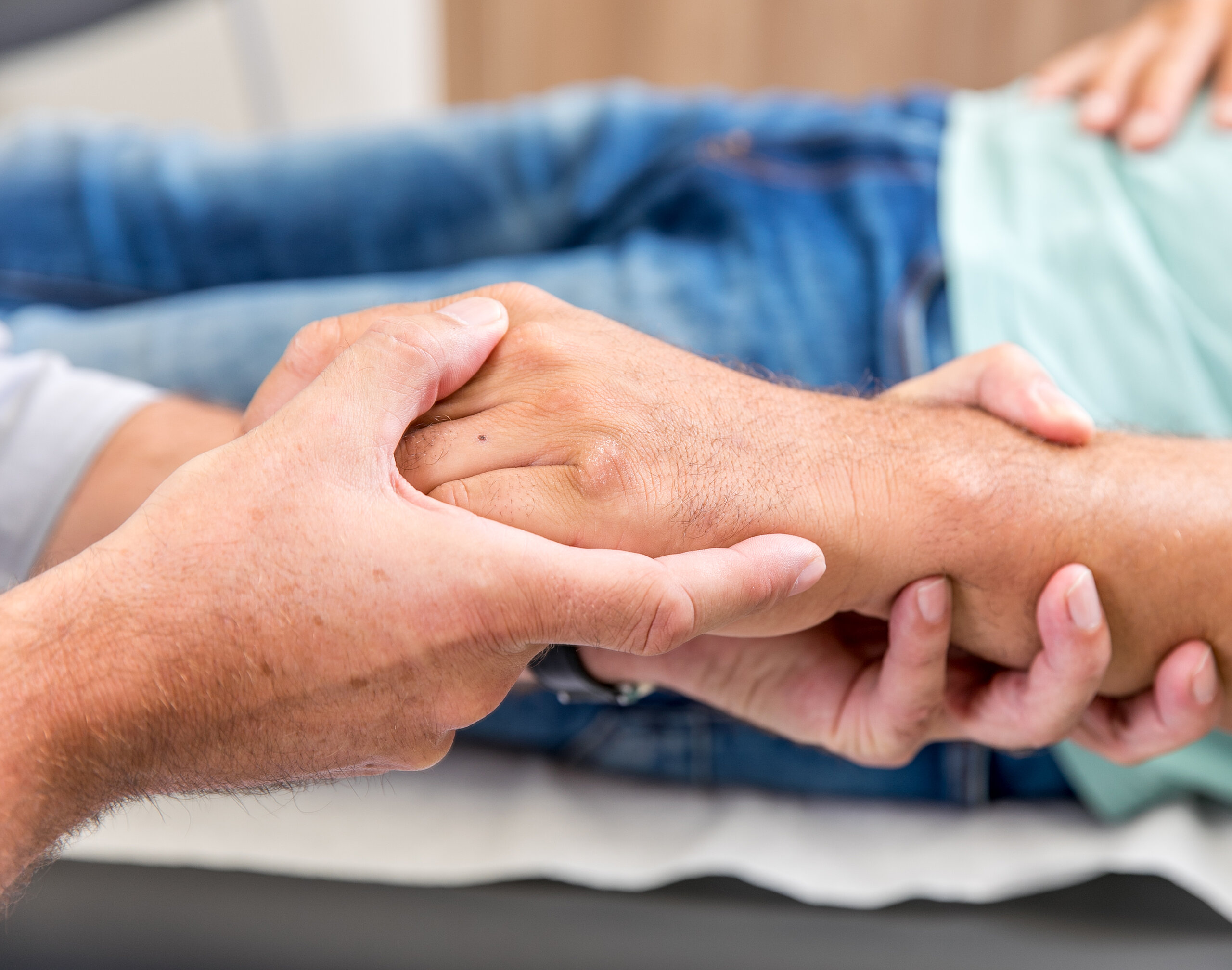 Zwei Personen halten sich die Hände, Symbol für Fürsorge, Vertrauen und menschliche Nähe.