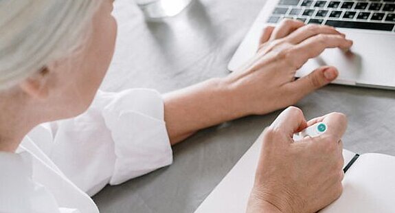 Frau am Laptop Eine ältere Frau sucht etwas am Laptop und macht sich dabei Notizen auf einen Block.