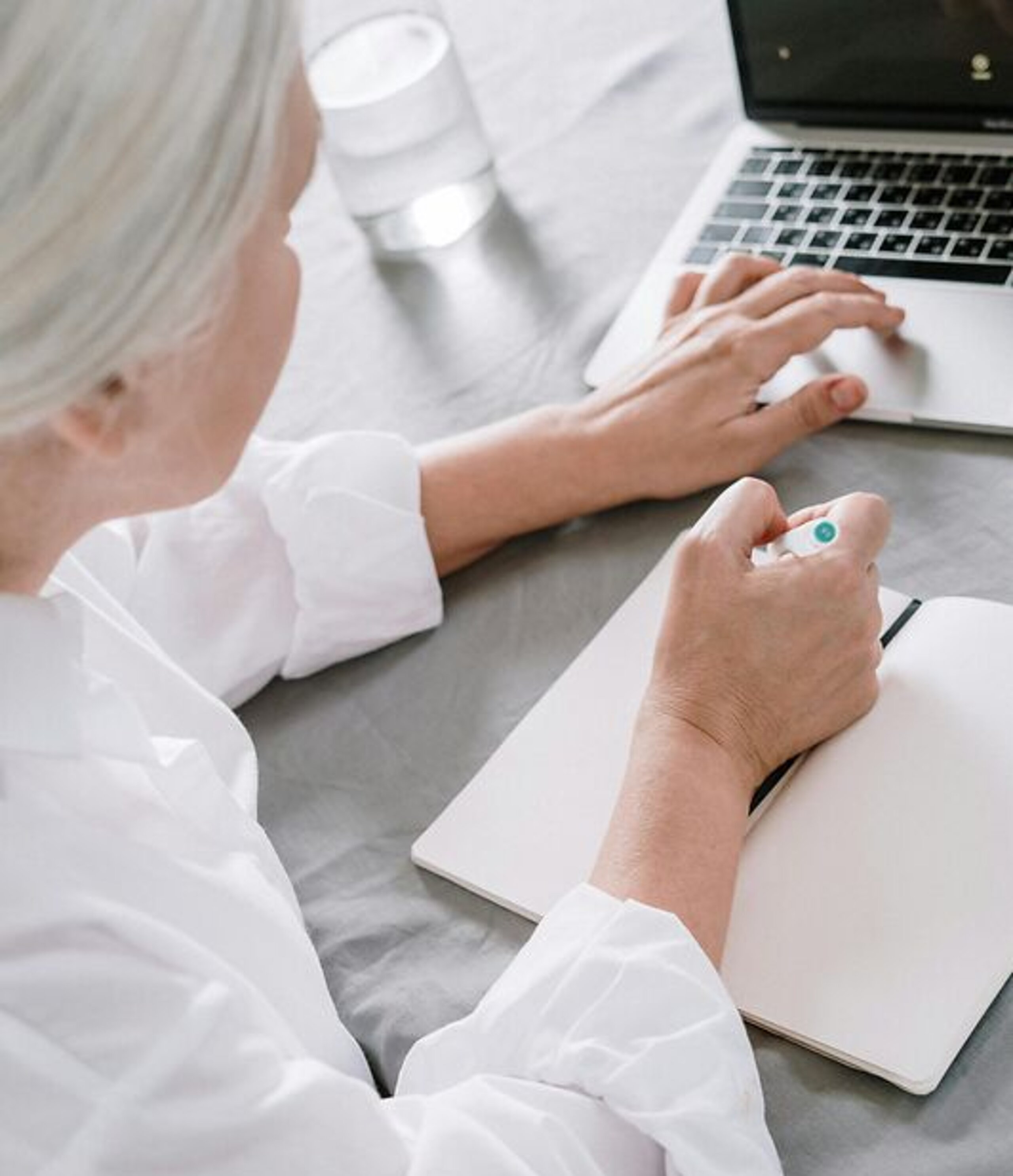 Frau am Laptop Eine ältere Frau sucht etwas am Laptop und macht sich dabei Notizen auf einen Block.