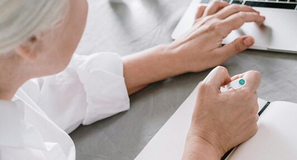 Frau am Laptop Eine ältere Frau sucht etwas am Laptop und macht sich dabei Notizen auf einen Block.