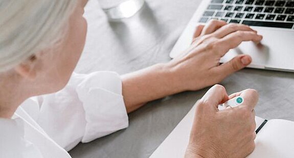 Frau recherchiert am Laptop Eine ältere Frau sucht etwas am Laptop und macht sich dabei Notizen auf einen Block.