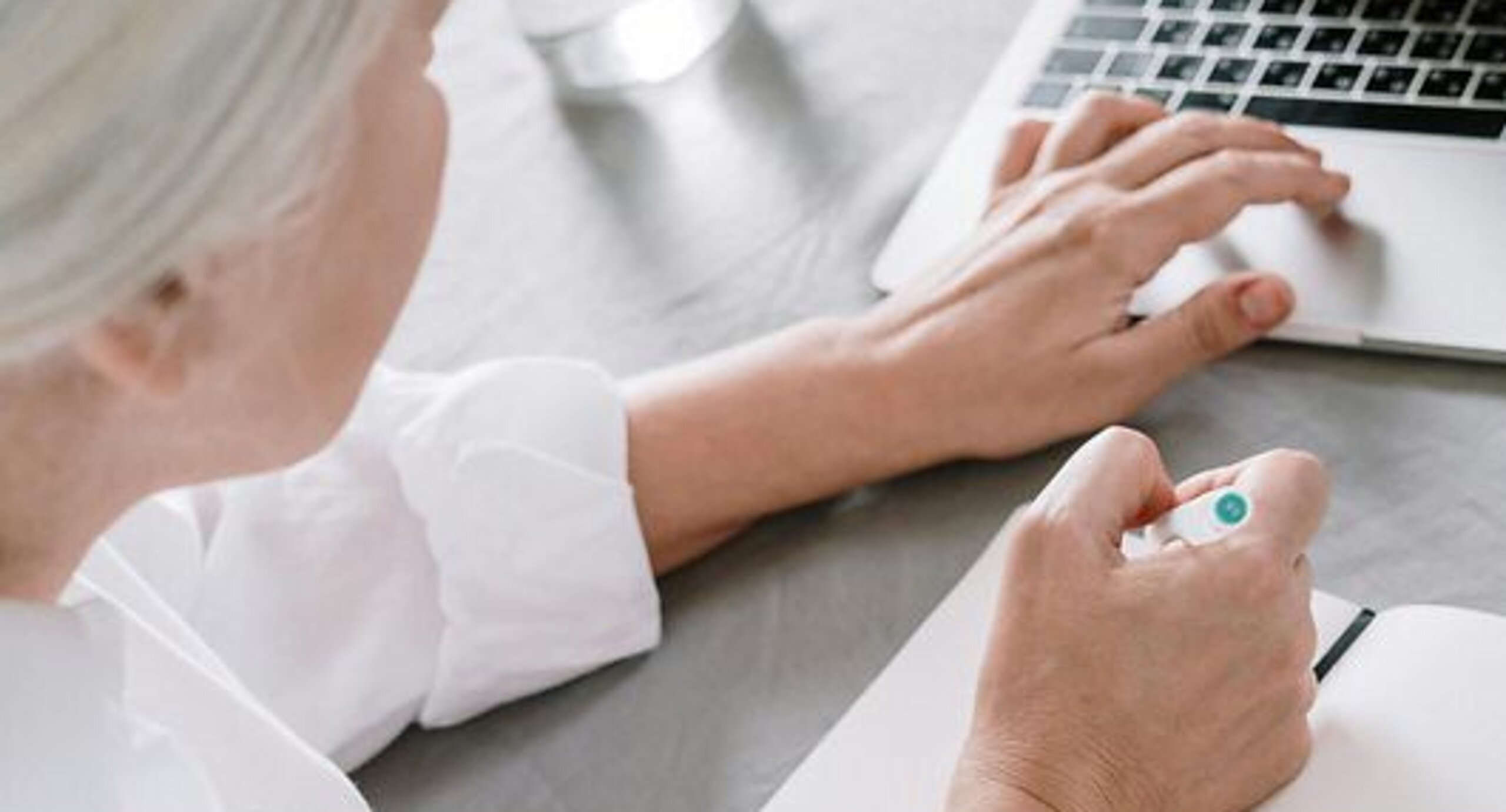 Frau am Laptop Eine ältere Frau sucht etwas am Laptop und macht sich dabei Notizen auf einen Block.