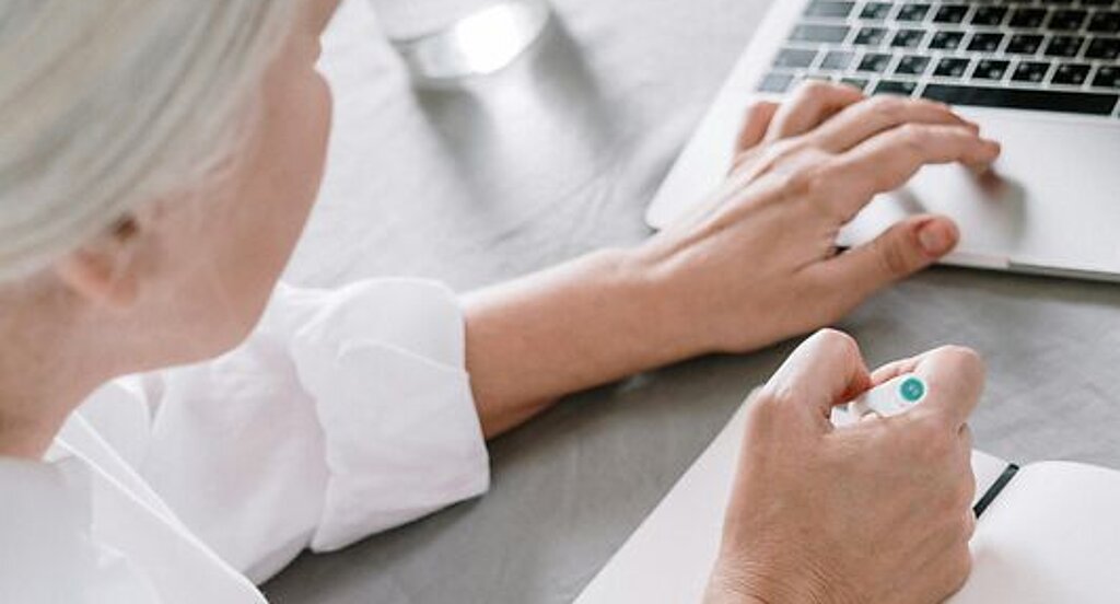 Frau recherchiert am Laptop Eine ältere Frau sucht etwas am Laptop und macht sich dabei Notizen auf einen Block.