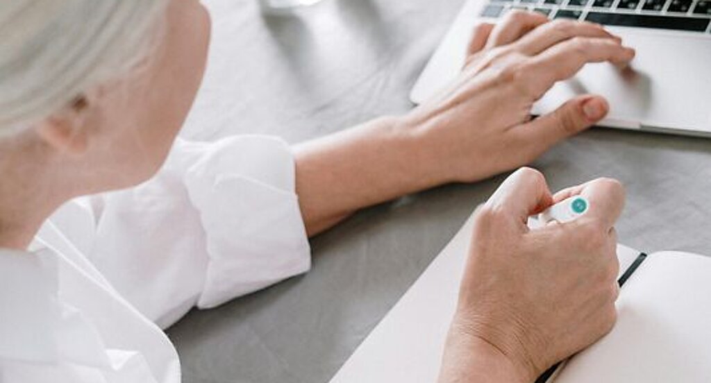 Frau am Laptop Eine ältere Frau sucht etwas am Laptop und macht sich dabei Notizen auf einen Block.