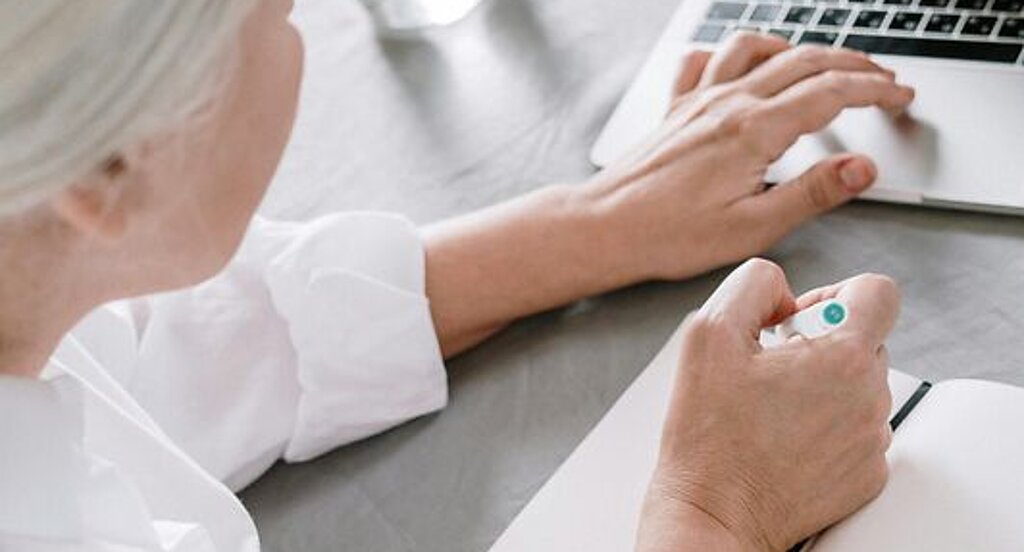 Frau am Laptop Eine ältere Frau sucht etwas am Laptop und macht sich dabei Notizen auf einen Block.