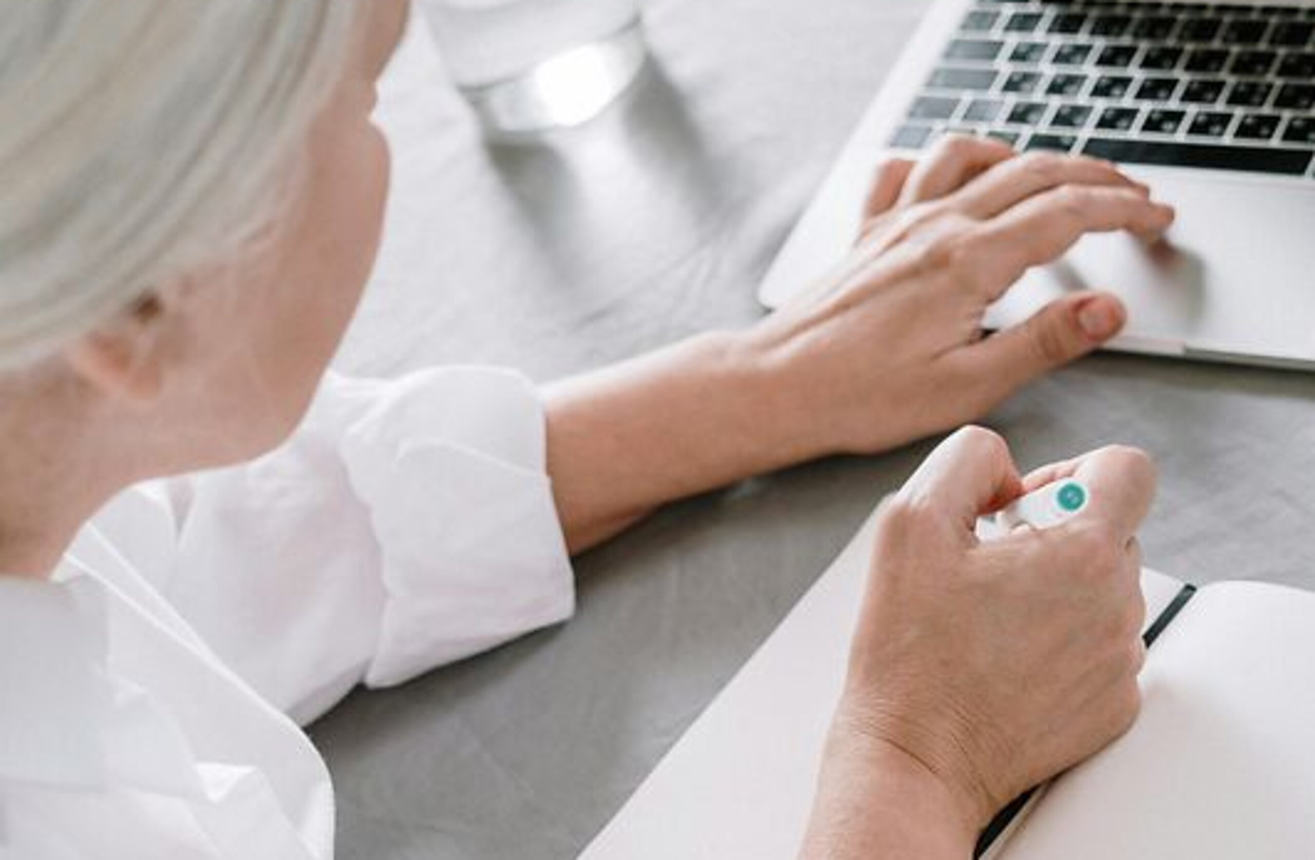 Frau am Laptop Eine ältere Frau sucht etwas am Laptop und macht sich dabei Notizen auf einen Block.