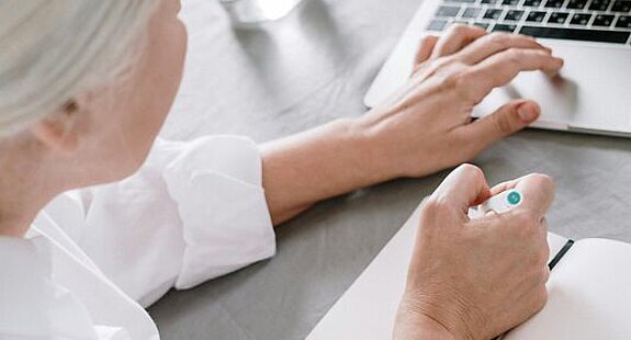 Frau am Laptop Eine ältere Frau sucht etwas am Laptop und macht sich dabei Notizen auf einen Block.