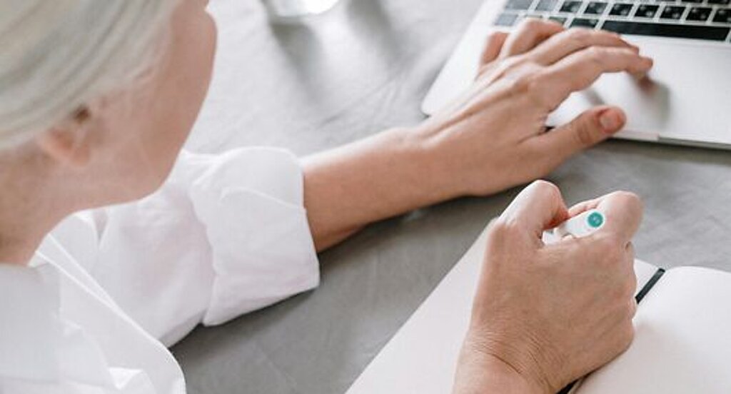 Frau am Laptop Eine ältere Frau sucht etwas am Laptop und macht sich dabei Notizen auf einen Block.