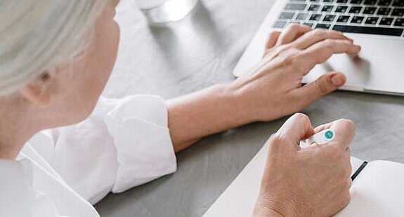 Frau recherchiert am Laptop Eine ältere Frau sucht etwas am Laptop und macht sich dabei Notizen auf einen Block.