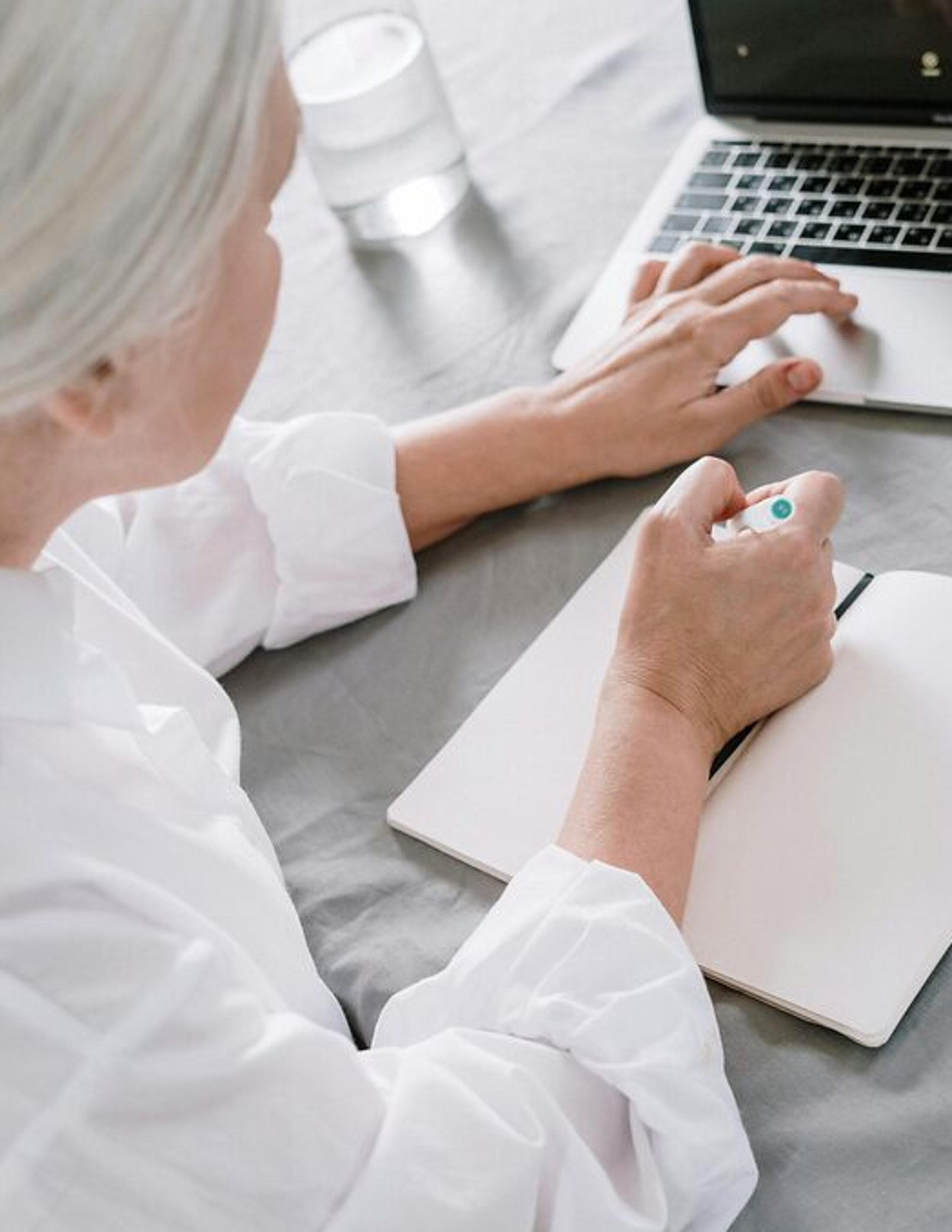 Frau am Laptop Eine ältere Frau sucht etwas am Laptop und macht sich dabei Notizen auf einen Block.