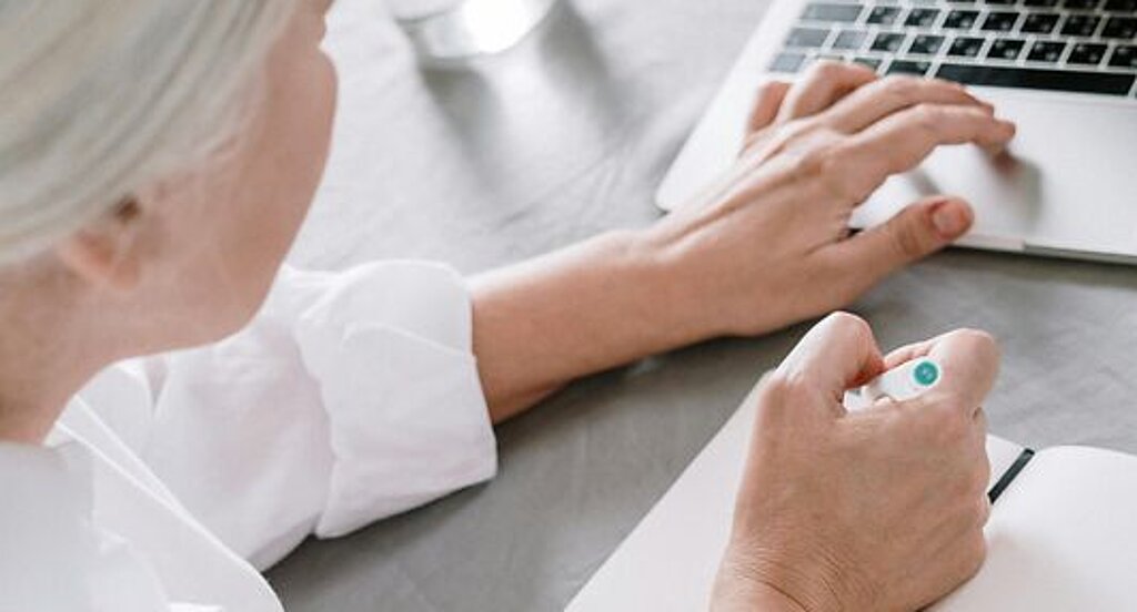 Frau recherchiert am Laptop Eine ältere Frau sucht etwas am Laptop und macht sich dabei Notizen auf einen Block.