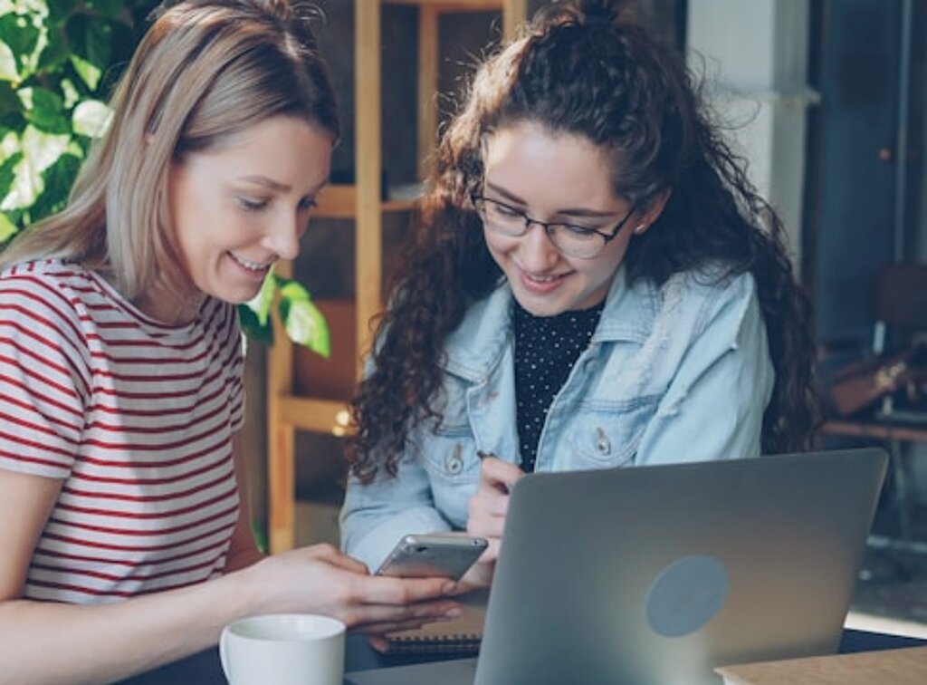 Studentinnen Zwei Studentinnen schauen gemeinsam in einen Laptop und ein Smartphone.