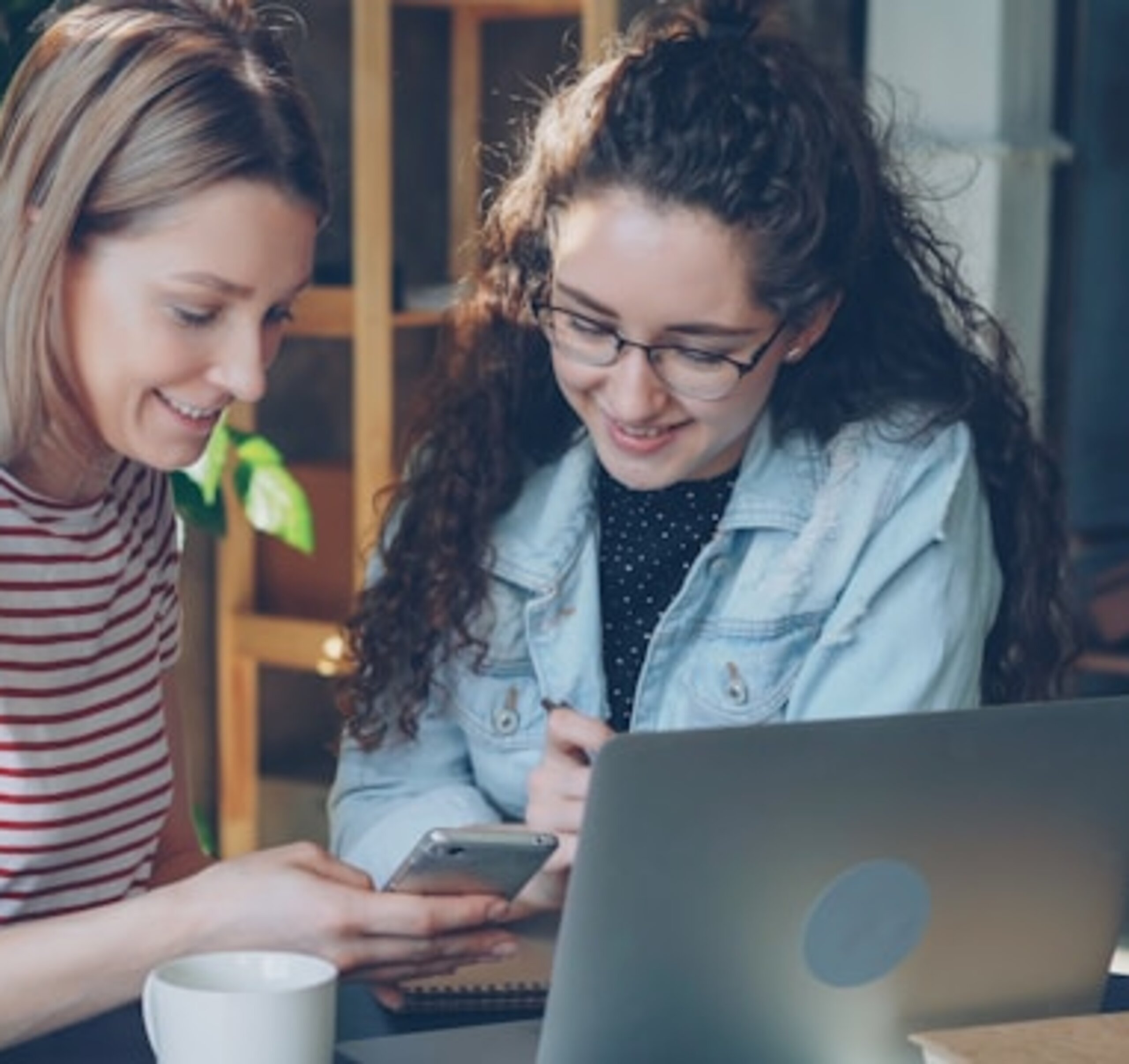 Zwei Studentinnen schauen gemeinsam in einen Laptop und ein Smartphone.