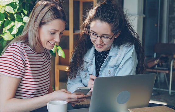 Studentinnen Zwei Studentinnen schauen gemeinsam in einen Laptop und ein Smartphone.