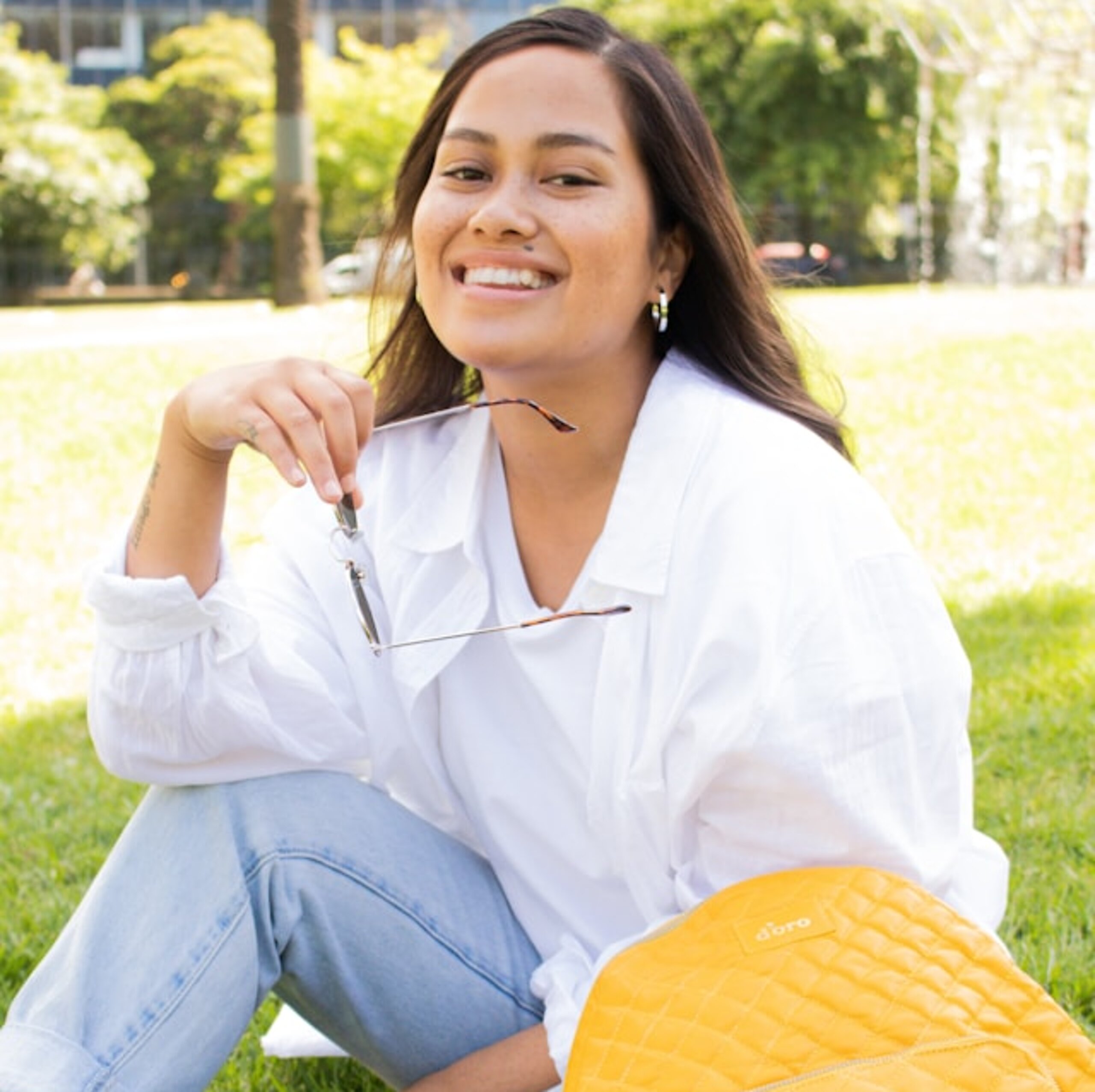 Eine Studentin sitzt lachend im Park mit Tasche.