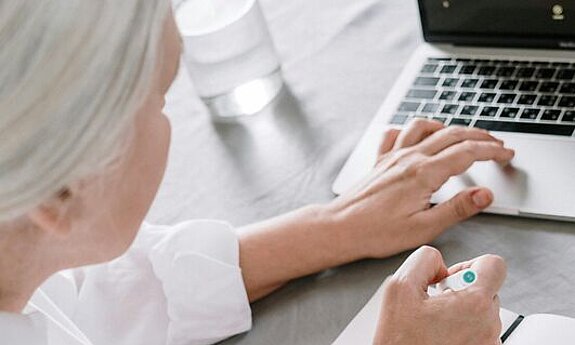 Eine Person recherchiert am Laptop und macht sich Notizen.