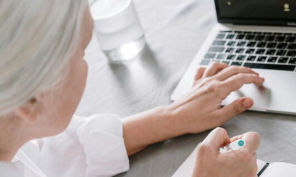 Eine Person recherchiert am Laptop und macht sich Notizen.