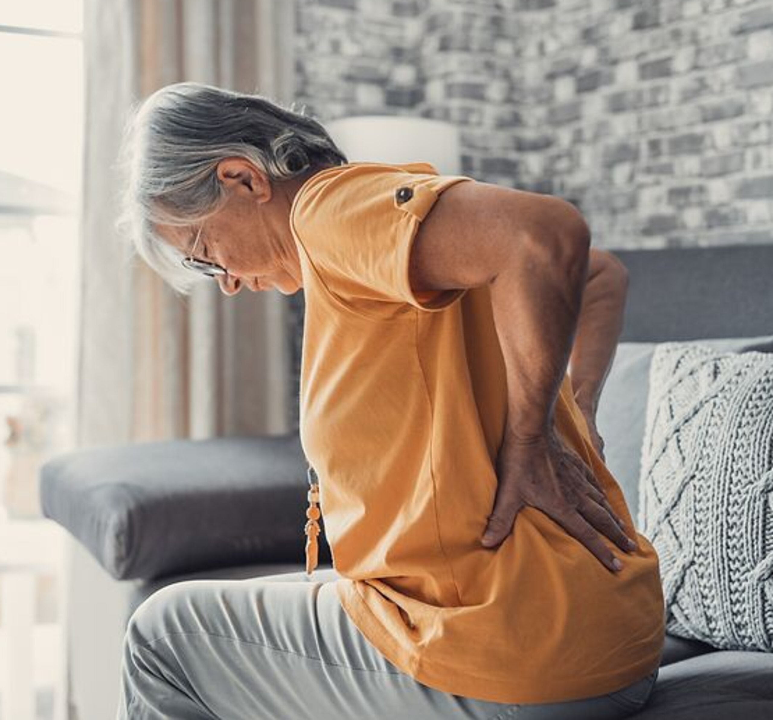 Frau mit Rückenschmerzen Eine ältere Frau hält sich schmerzhaft die Hände an den unteren Rücken.