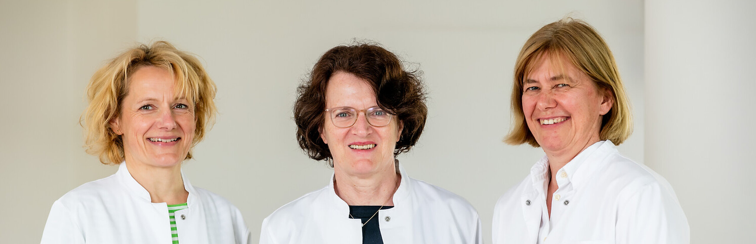 Drei Ärztinnen mit weißem Kittel lächeln in die Kamera.