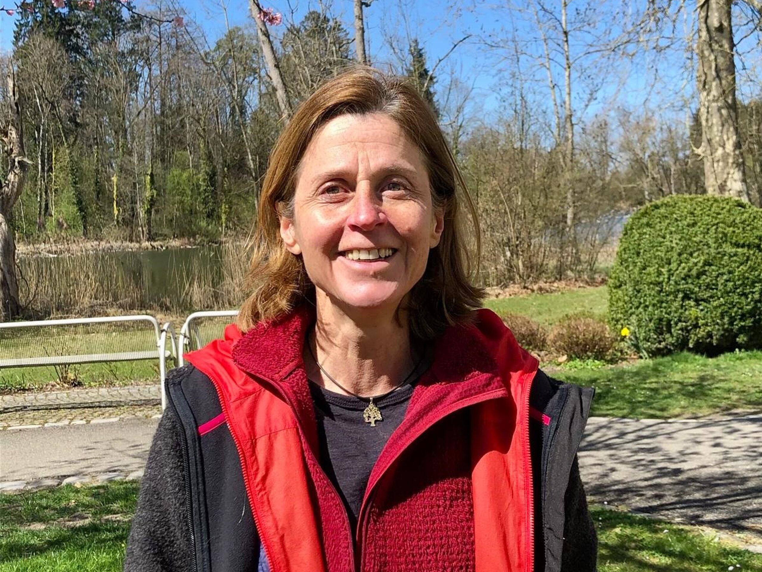 Patientin der Klinik im Hofgarten lächelt in die Kamera, im Hintergrund ist der Schlosssee zu sehen.