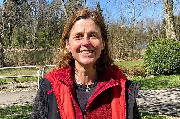 Patientin der Klinik im Hofgarten lächelt in die Kamera, im Hintergrund ist der Schlosssee zu sehen.