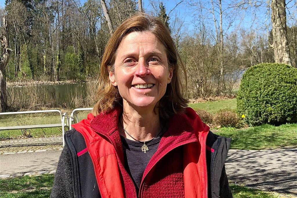 Patientin der Klinik im Hofgarten lächelt in die Kamera, im Hintergrund ist der Schlosssee zu sehen.