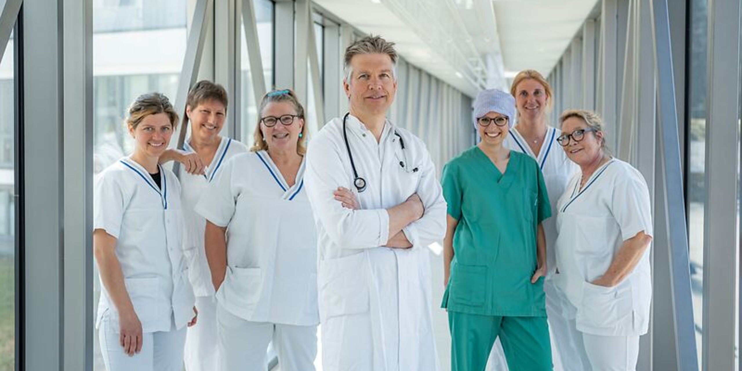 Arzt und ein Team aus Pflegekräften stehen gemeinsam in einem hellen Glasgang.