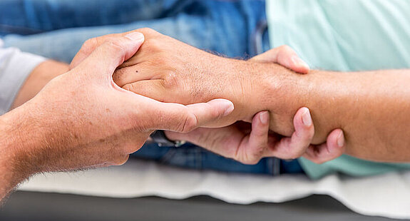 Ein Arzt umfasst die Hand eines Patienten.