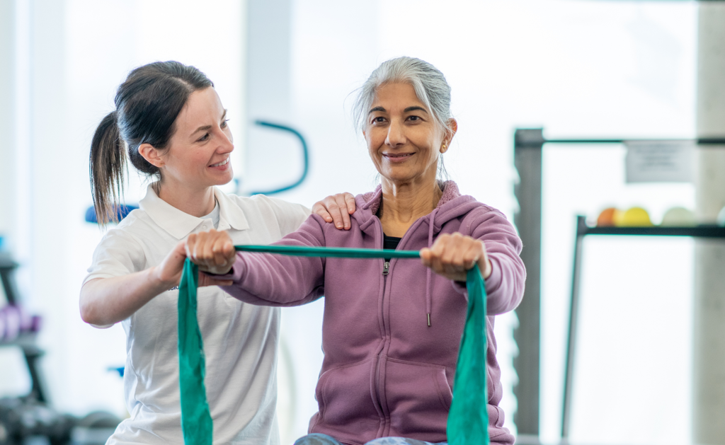 Physiotherapie mit Ball Eine Therapeutin unterstützt eine Patientin bei Übungen mit dem Therraband.