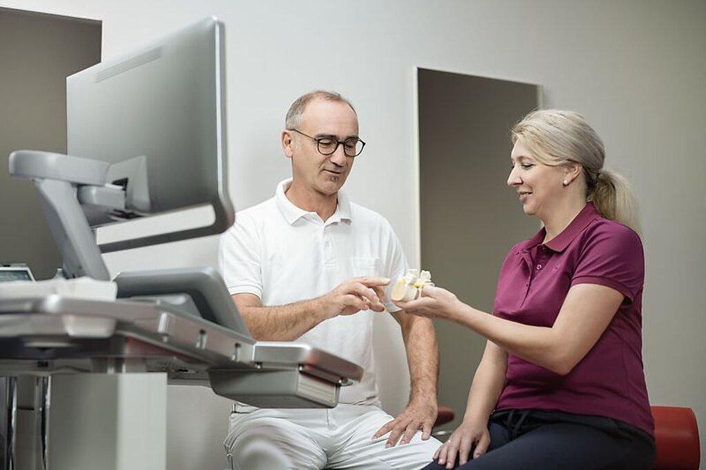 Ein Arzt erklärt einer Patientin etwas an einem Knochenmodel.