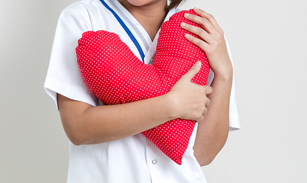 Eine Pflegerin hält ein rotes Herzkissen in der Hand.