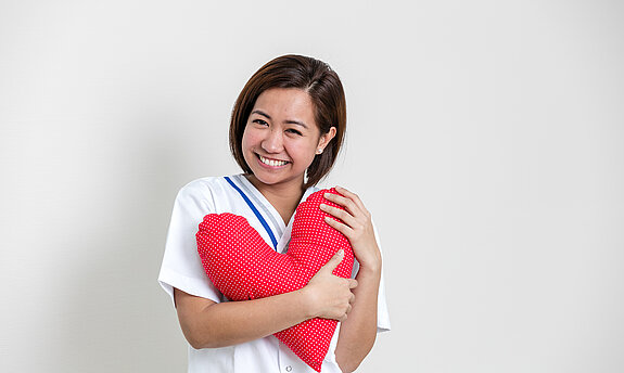 Eine Pflegerin hält ein rotes Herzkissen in der Hand.