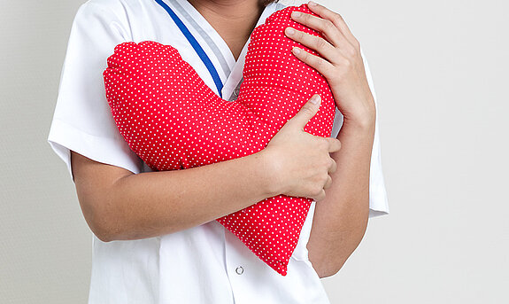 Eine Pflegerin hält ein rotes Herzkissen in der Hand.