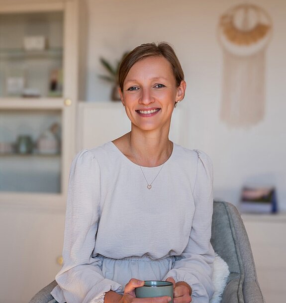 Monika Resch sitzt lächelnd in ihrer Praxis.