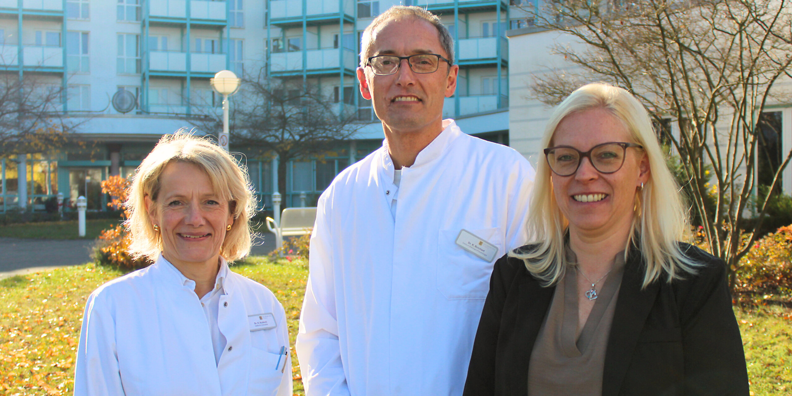 Die Klinikleitung - bestehend aus der orthopädischen Chefärztin, dem onkologischen Chefarzt sowie der kaufmännischen Leiterin - lächeln in die Kamera.